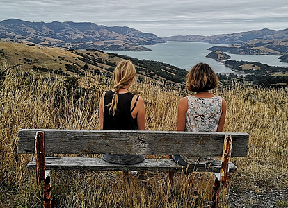 Zwei Mädchen sitzen auf einer Bank und schauen ins Tal