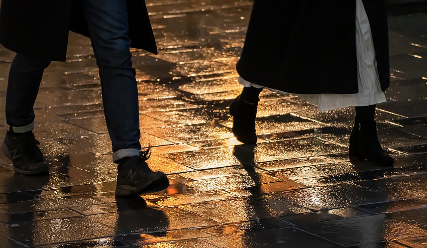 Mann und Frau laufen im Regen über eine Straße