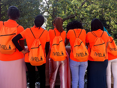 Rückenansicht von sechs Frauen in orangen T-Shirts mit orangen Rucksäcken
