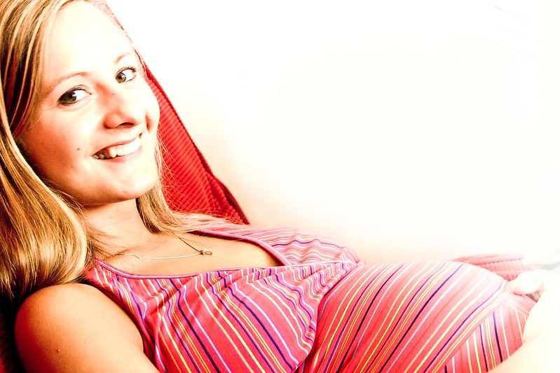 Blonde Frau, schwanger, liegt und lächelt in die Kamera